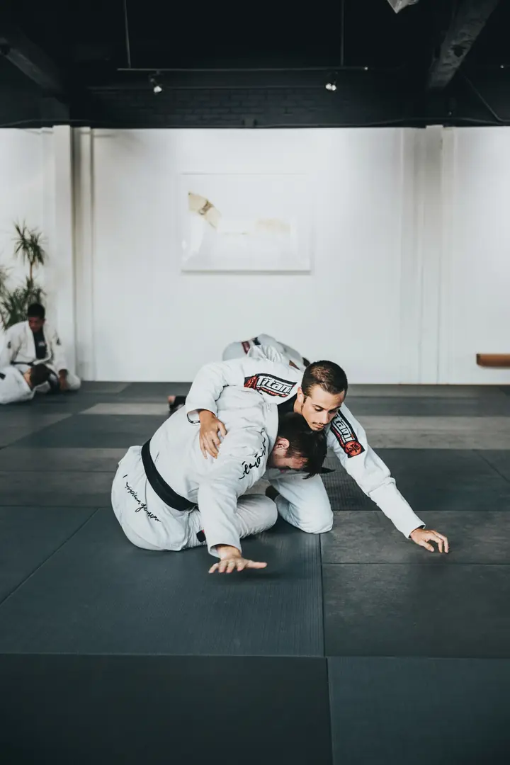 Two athletes in white gis grappling in a bright martial arts academy