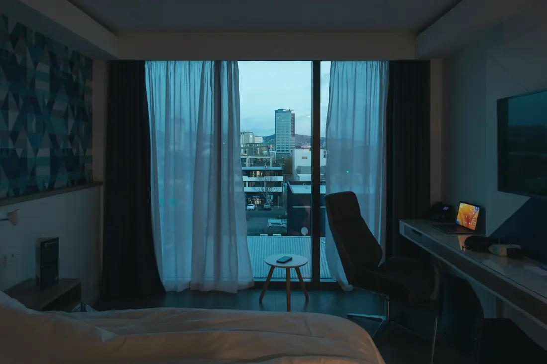 A quiet hotel room with sheer curtains and a city view at dusk