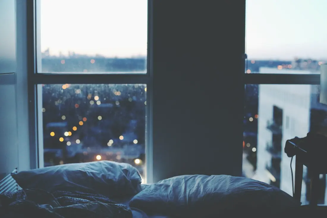 Pillows on a bed beside a window at dusk