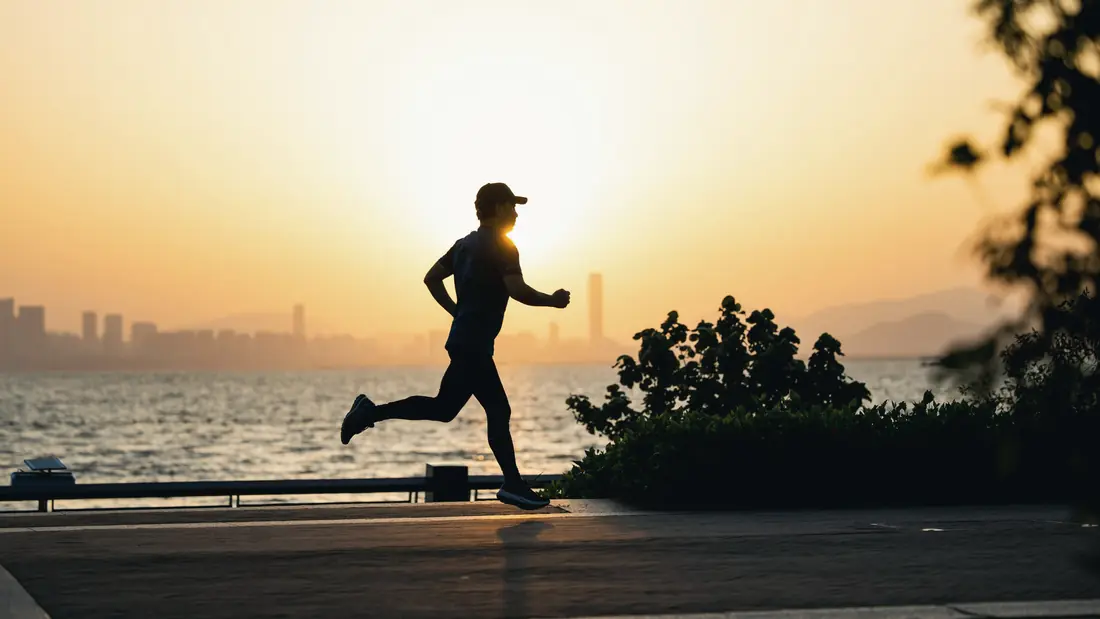 A runner silhouetted against a sunrise along a waterfront path